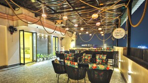 An indoor seating area with black wicker chairs, potted plants, and a bar counter. - Orsom Stays Sassy Sector 53 (Gurugram)