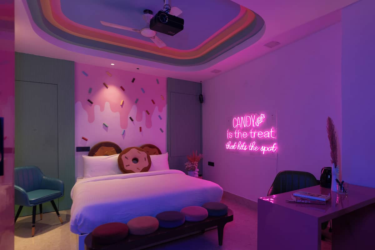 Une chambre moderne avec un lit, des oreillers, un ventilateur de plafond, un néon et un bureau avec un livre.