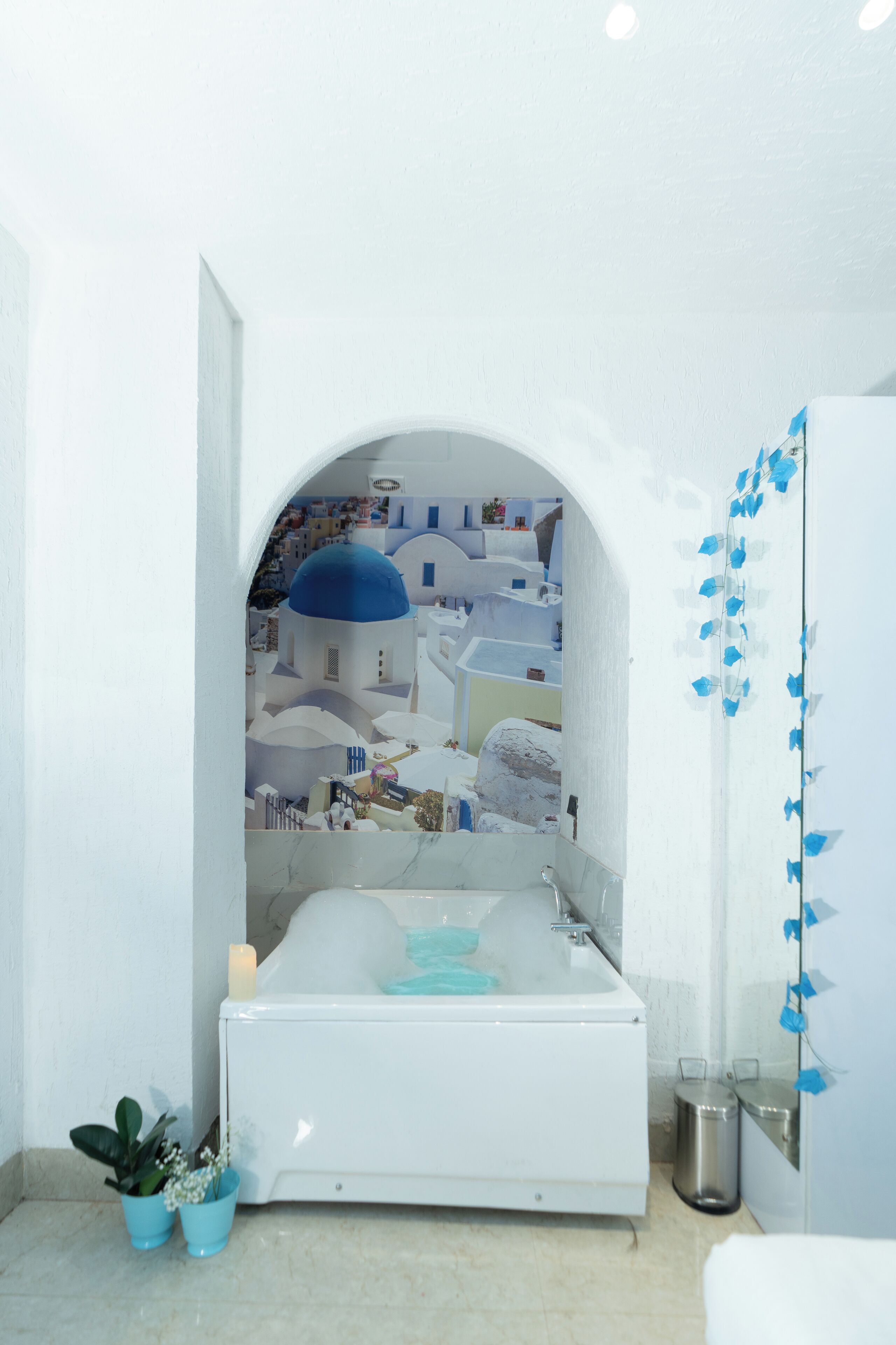 A bathroom with a bathtub, a sink, and a mirror. There is a potted plant and a trash can.