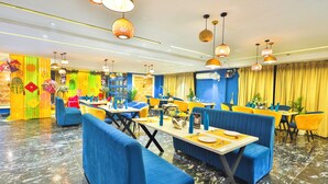 A restaurant with blue booths, yellow tables, and hanging lamps. - Orsom Stays Sassy Sector 53 (Gurugram)