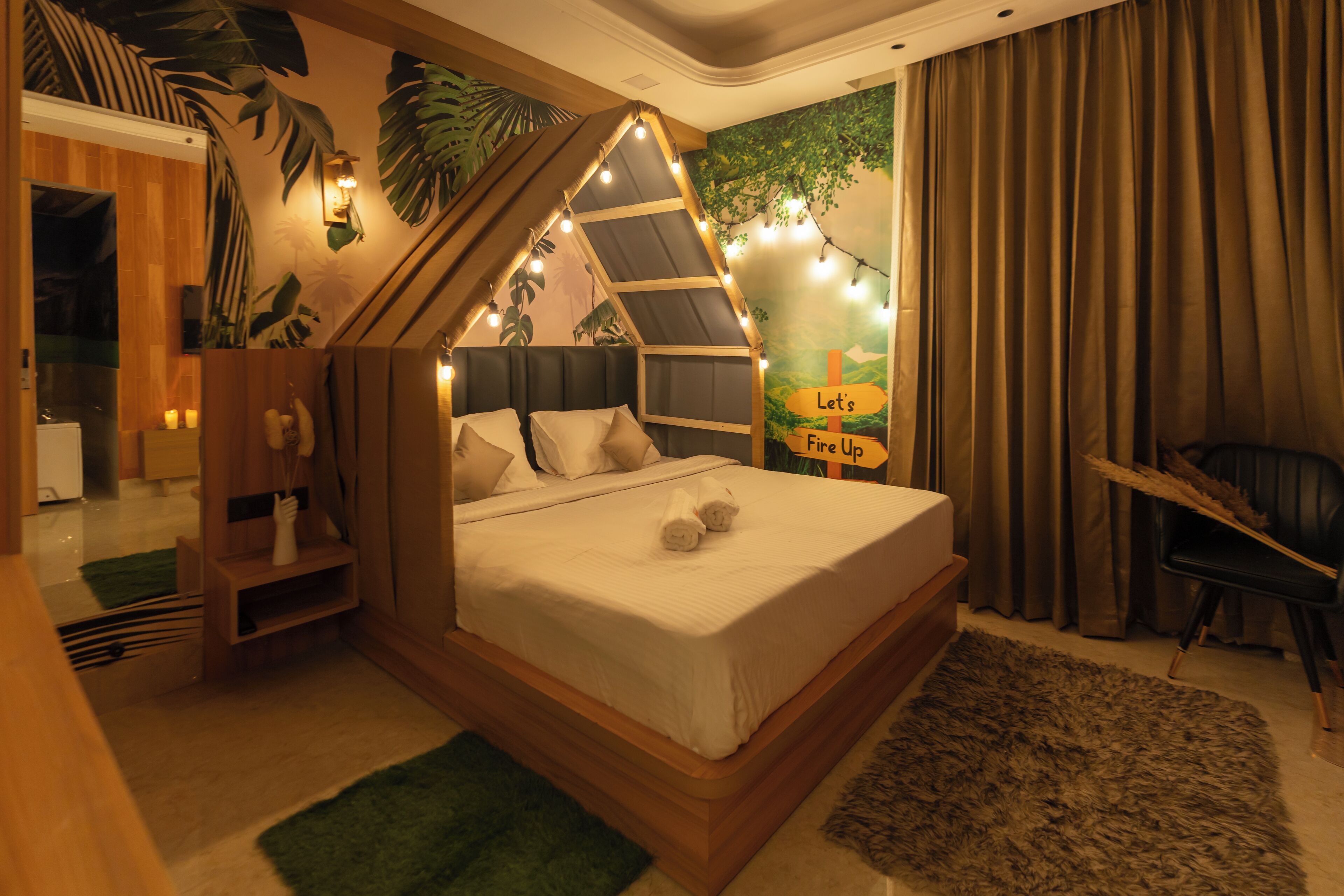 A bedroom with a bed, a wooden headboard, a green rug, a chair, and a wall with a mural.