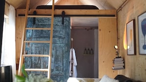 A cozy room with a wooden ceiling, a ladder, a door, and a shelf with books and a lamp. - Off-grid Cork Cabin With It's Own Island (Gillingham)