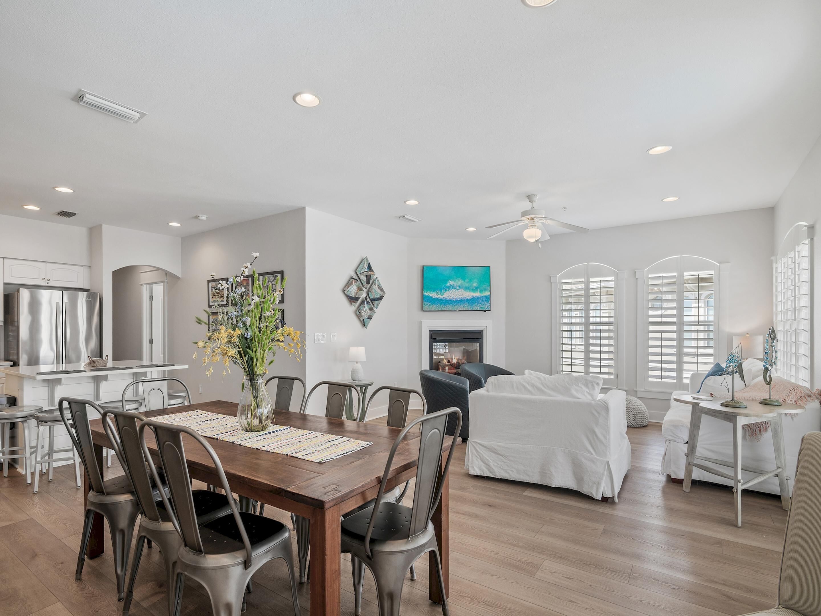A spacious living area with a dining table, chairs, a fireplace, and a large window with shutters.