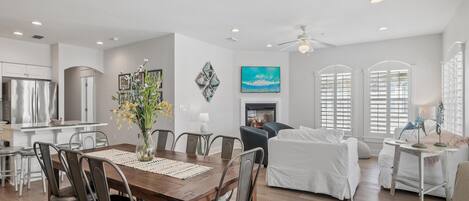 A spacious living area with a dining table, chairs, a fireplace, and a large window with shutters.