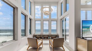 A spacious room with large windows overlooking the ocean, a built-in bookshelf, and a television on the right. - Sugar Sands Sanctuary: Breathtaking Beach Views, Private Pool, 6 Bedrooms ! (St. George Island)