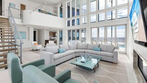 A spacious living area with a large sectional sofa, a glass coffee table, and a staircase leading to an upper level. - Sugar Sands Sanctuary: Breathtaking Beach Views, Private Pool, 6 Bedrooms ! (St. George Island)