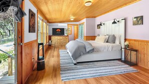 Un dormitorio con techo de madera, una cama con ropa de cama gris, un tapete a rayas y una pequeña mesita de noche con un jarrón.
