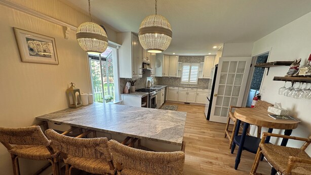 Una cocina con isla de mármol, sillas de mimbre, lámparas colgantes y una mesa de comedor.