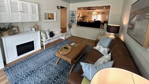 Una sala de estar con chimenea, paredes de ladrillo blanco, un sofá y un comedor con vista a la cocina.