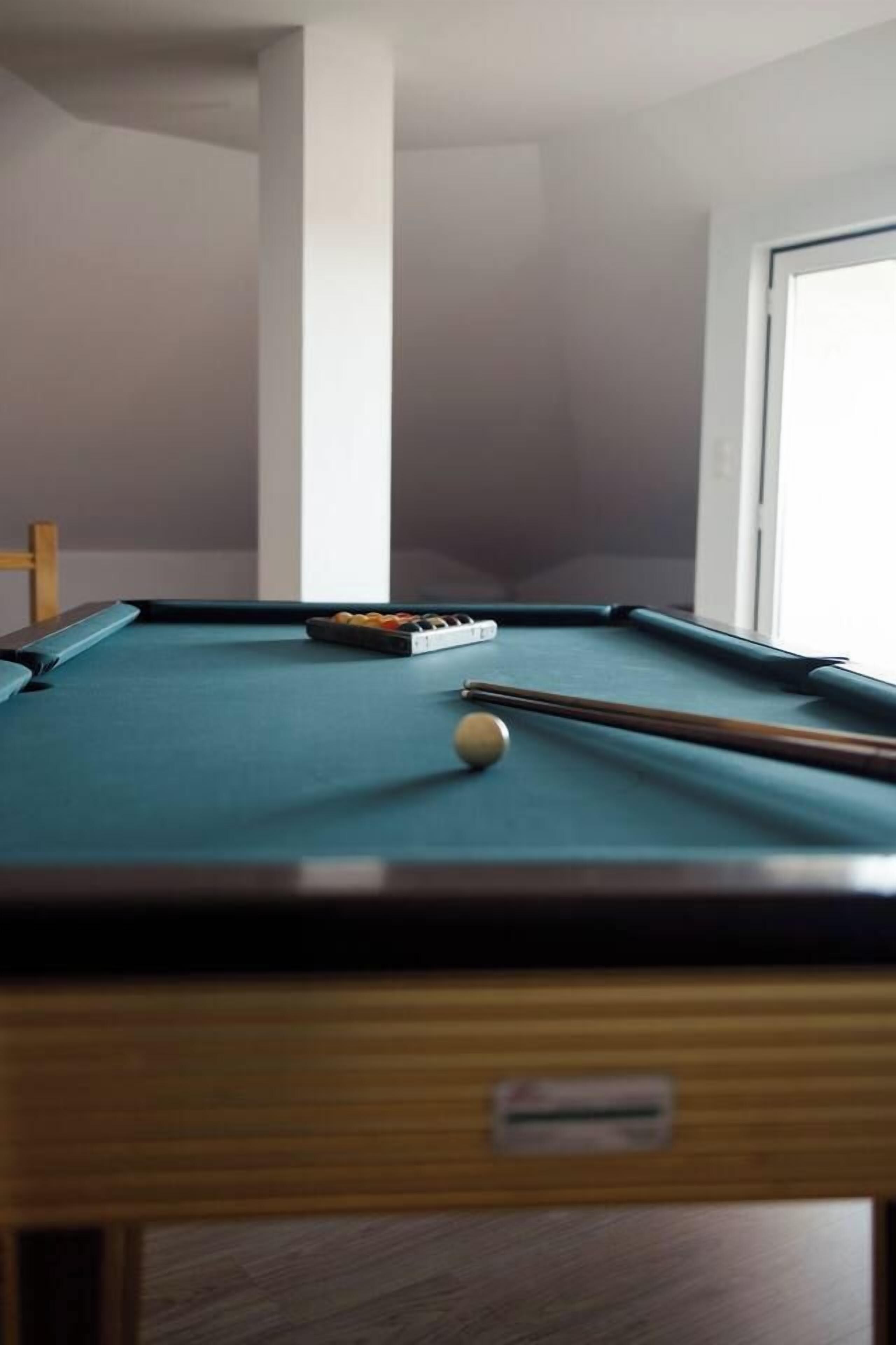 Una mesa de billar con taco y bolas, una silla de madera y una puerta al fondo.