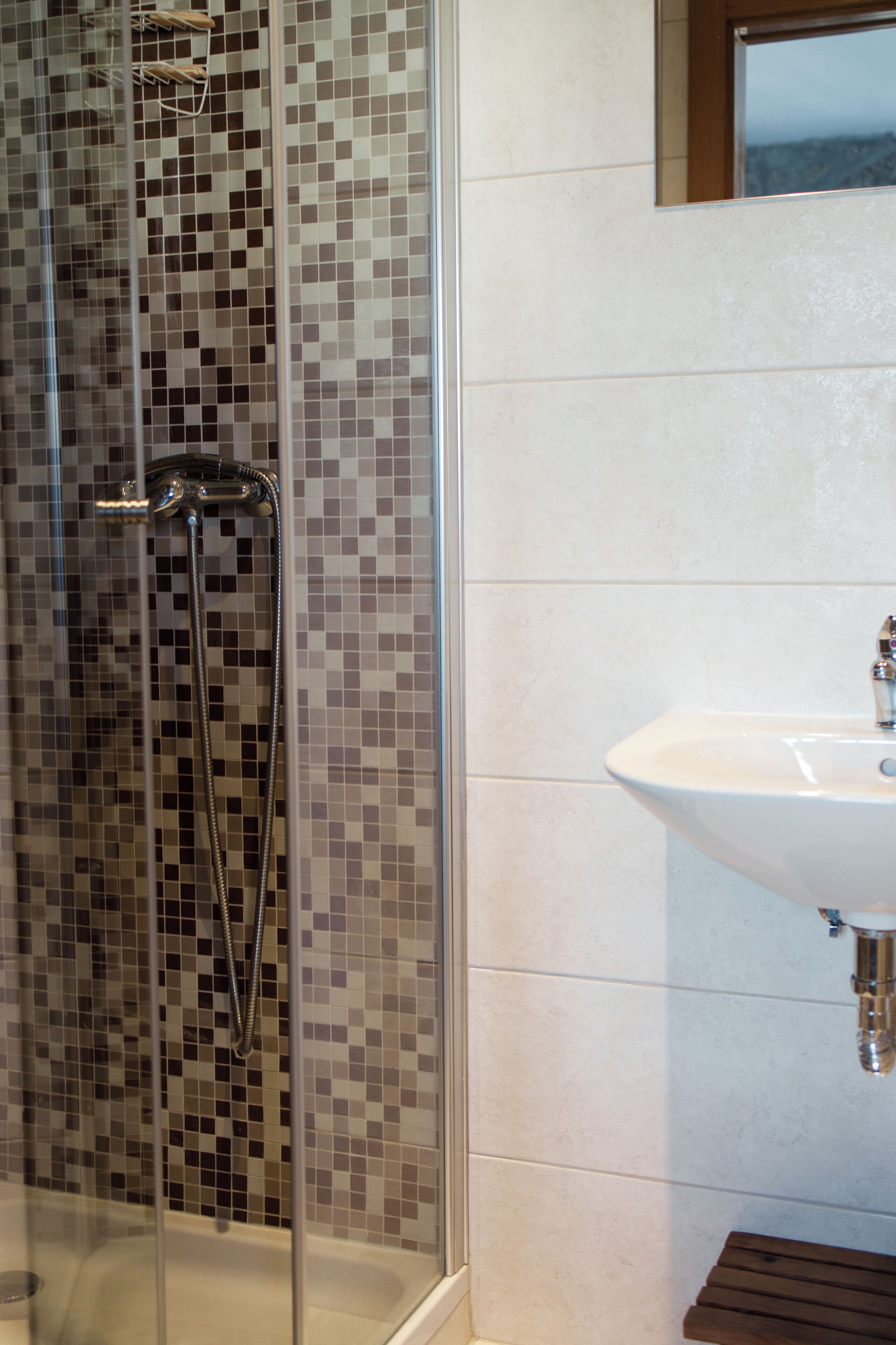 A bathroom with a glass-enclosed shower, a white sink, and tiled walls.