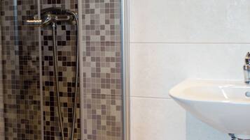 A bathroom with a glass-enclosed shower, a white sink, and tiled walls.