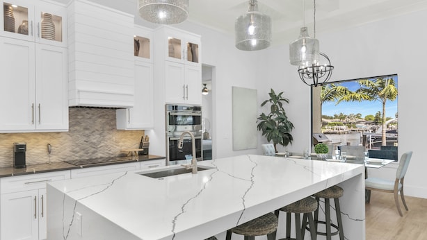 Une cuisine moderne avec des meubles blancs, un îlot en marbre et des luminaires suspendus.