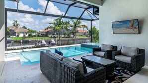 Un espace extérieur abrité, doté d’une piscine, de meubles en osier et offrant une vue sur un quartier résidentiel.