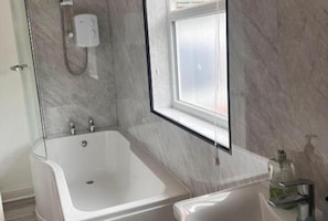 Une salle de bain moderne équipée d’une baignoire, d’une douche, d’une fenêtre et d’un lavabo avec un distributeur de savon.
