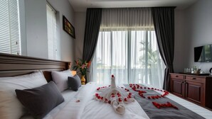 A hotel room with a neatly made bed, a large window with curtains, a flat-screen TV, and a wooden headboard. - Angkor Lany Sinit Resort (Siem Reap)