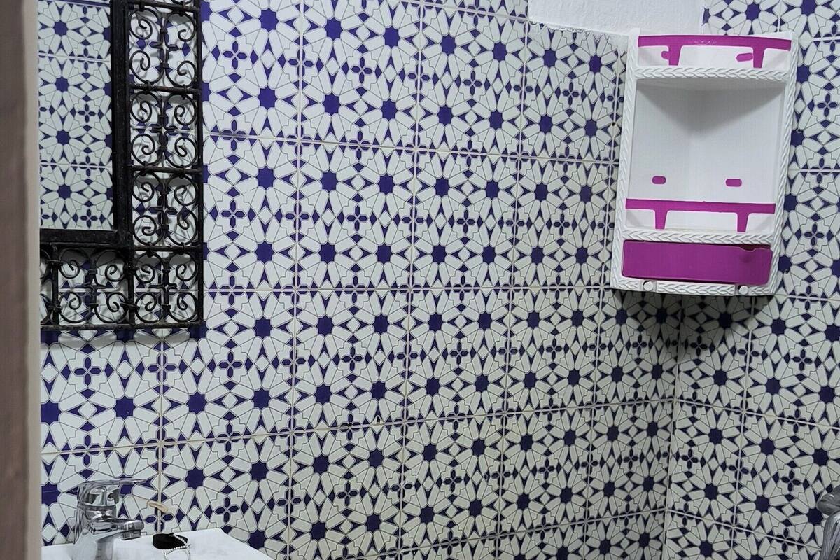 A bathroom with a white sink, a shower, and a patterned tile wall.