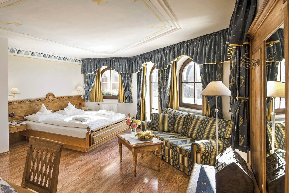 Habitación de hotel con una cama grande, un sofá, una silla de madera y una mesa con una lámpara.