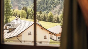 Een kamer met een groot rondboogvenster met uitzicht op een bergachtig landschap en een gebouw met een schuin dak.