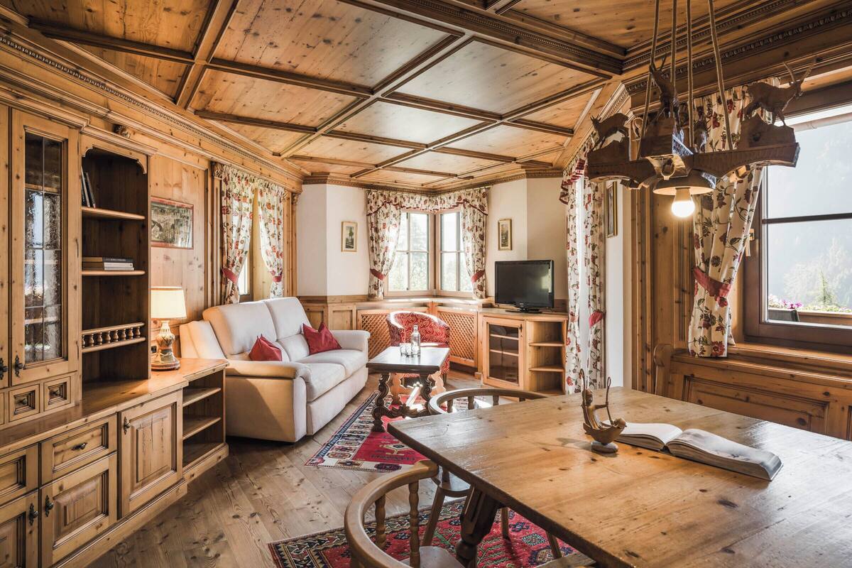 Una habitación acogedora y rústica con techos y paredes de madera, un sofá, un televisor y una mesa de comedor con un tapete rojo.