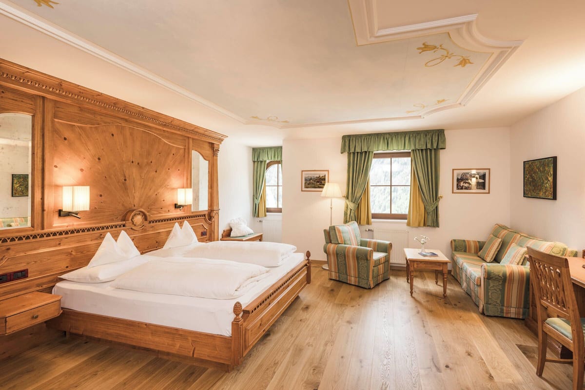 Habitación de hotel con una cama grande de madera, un escritorio de madera, una silla, un sofá y una mesita.