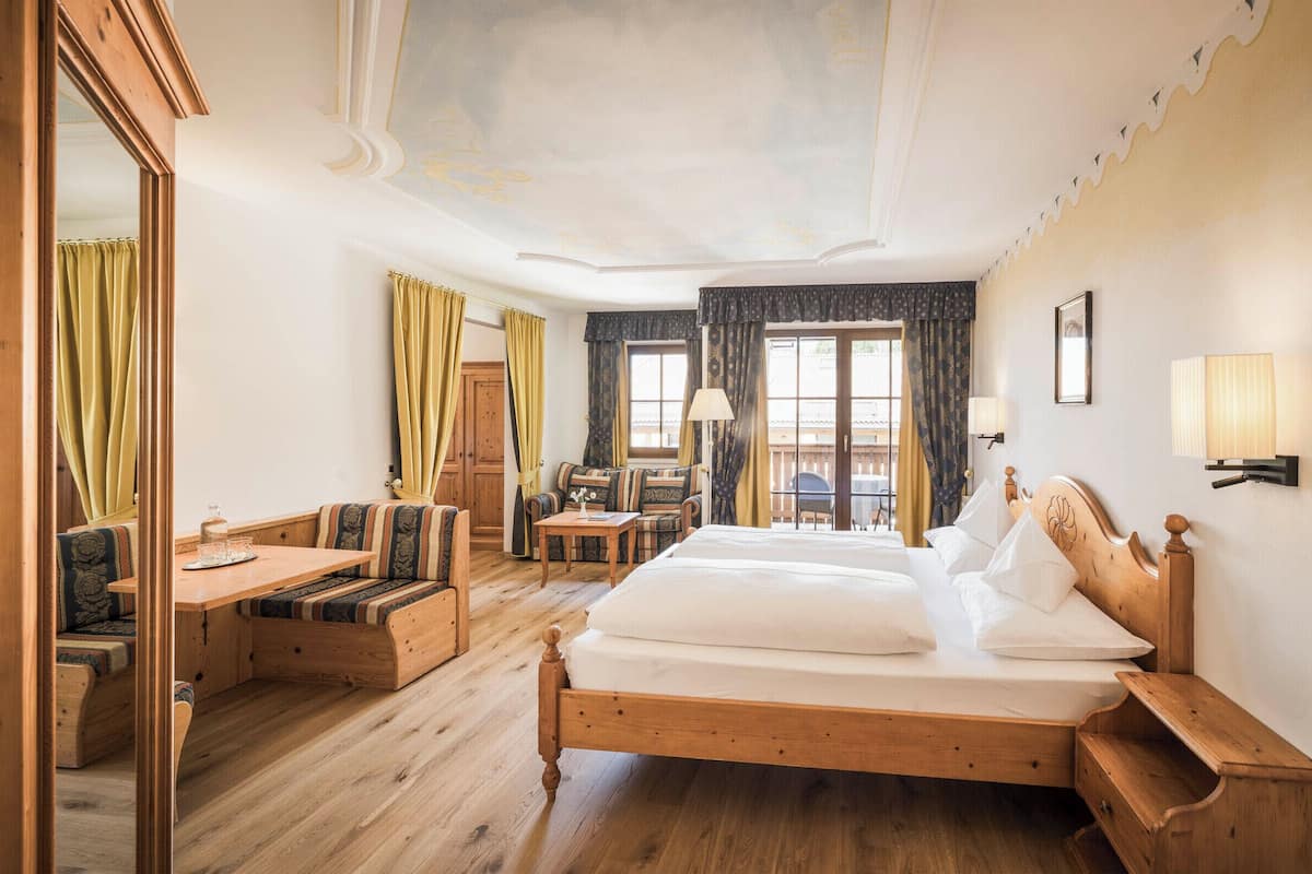 Una habitación de hotel con una cama de madera, un sofá, una mesita y un espejo.