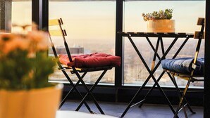 A balcony with two chairs, one with a red cushion and the other with a blue cushion, and a potted plant on a small table.