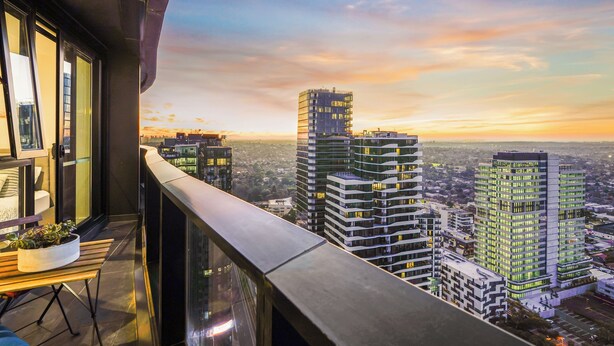 A balcony with a view of high-rise buildings and a sunset.