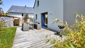 A wooden deck with outdoor furniture, a barbecue grill, and a sliding glass door leading to a covered patio.
