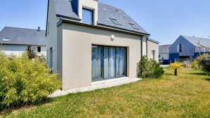 A modern two-story house with a sloped roof, large sliding glass doors, and a small balcony.