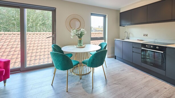 Una cocina moderna con una mesa redonda, sillas color turquesa y un ventanal grande.