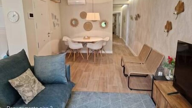 A modern living room with a sofa, a coffee table, and a TV stand. There is a dining area with a table and chairs. - Spacious, modern apartment located just outside the historic center. (Málaga)