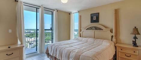 A bedroom with a bed, a nightstand, a lamp, and a view of the outside.