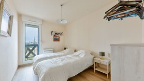 A bedroom with two beds, a small bedside table with a lamp, a window with a view of a bridge, and a coat rack with hangers. - Crouesty Harbor, flat with a pool for 4 (Arzon)