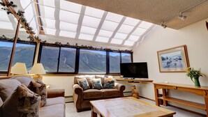 A living room with a large window, a sofa, a coffee table, and a television. - Vs741 Village Sqaure 3 Bedroom Condo by RedAwning (Copper Mountain)