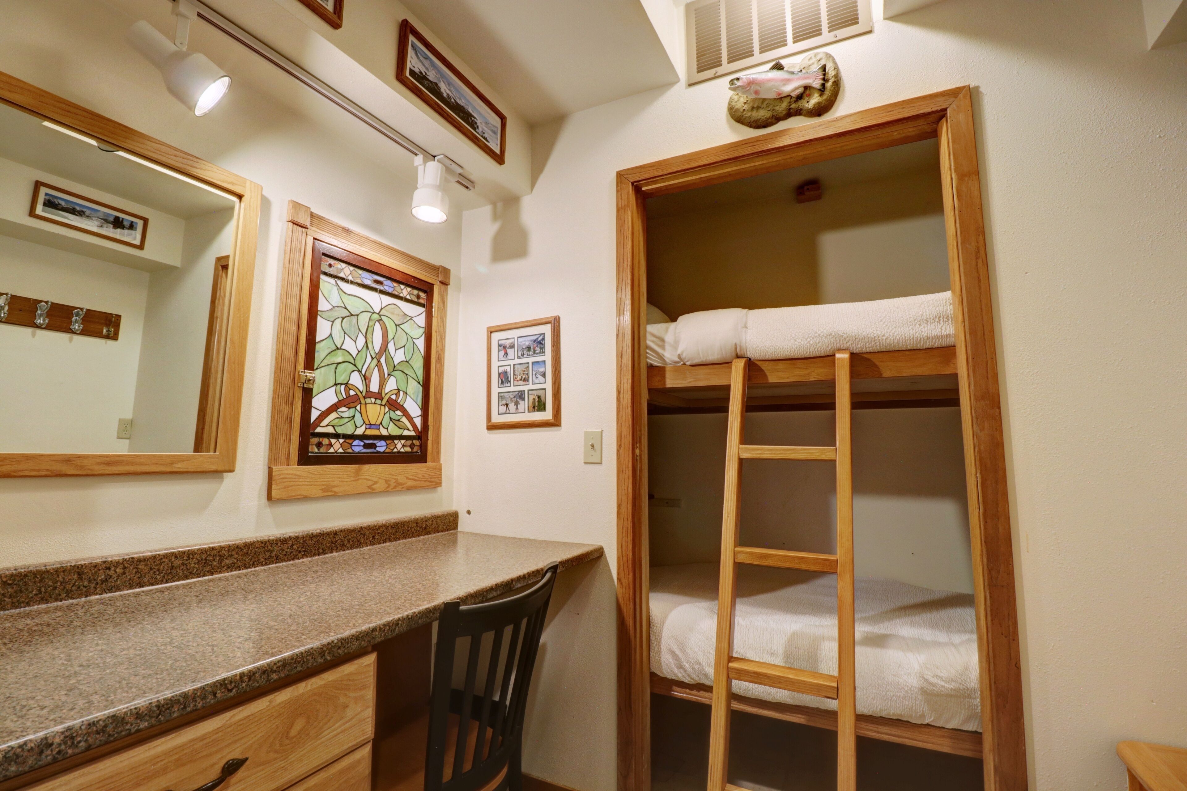A room with a wooden bunk bed, a granite countertop, a chair, and a stained glass window.