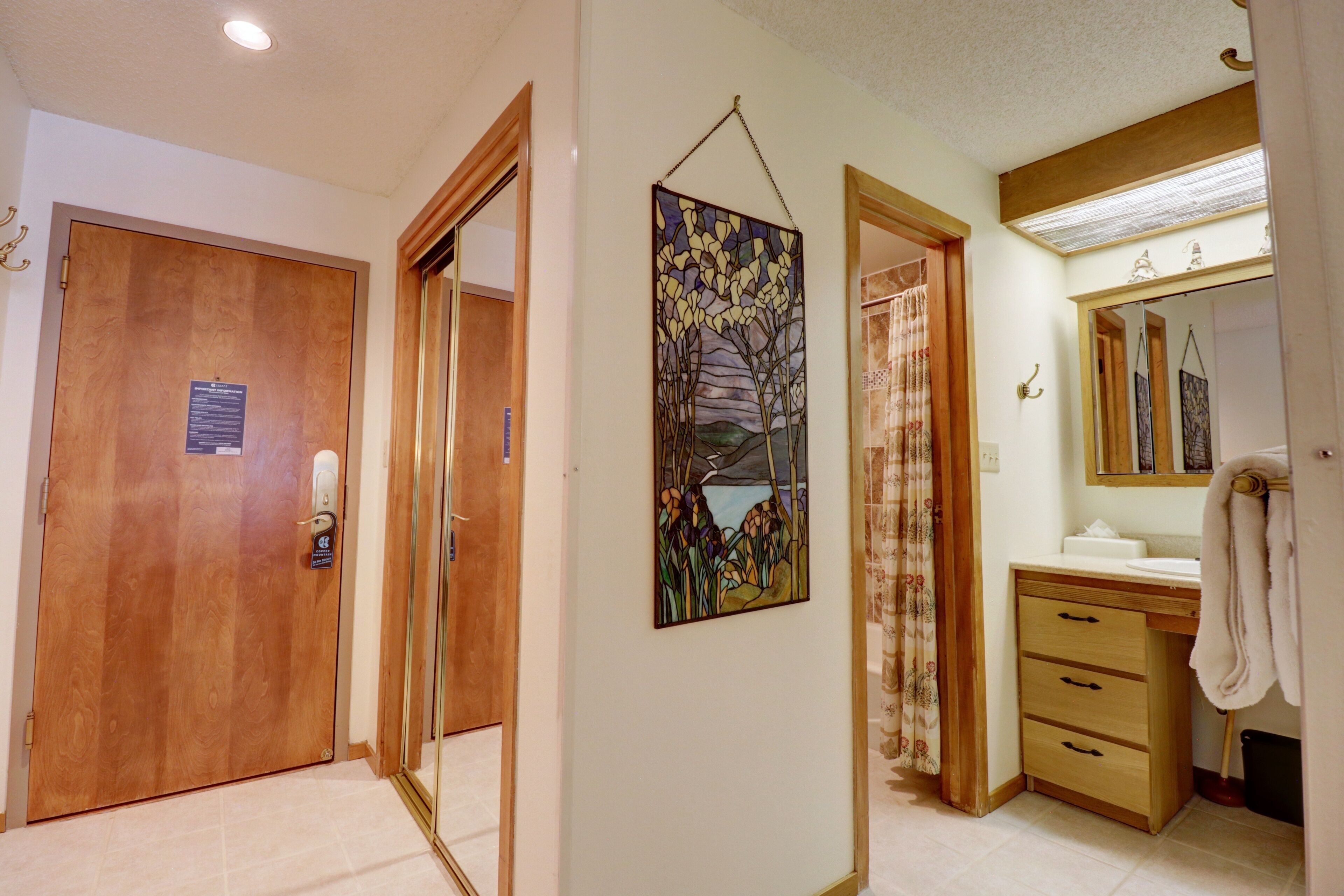 A bathroom with a wooden door, a painting of a landscape, a mirror, and a towel rack.