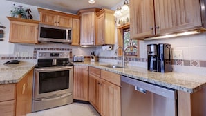 A kitchen with wooden cabinets, stainless steel appliances, a granite countertop, and a backsplash with a tile pattern. - Vs741 Village Sqaure 3 Bedroom Condo by RedAwning (Copper Mountain)