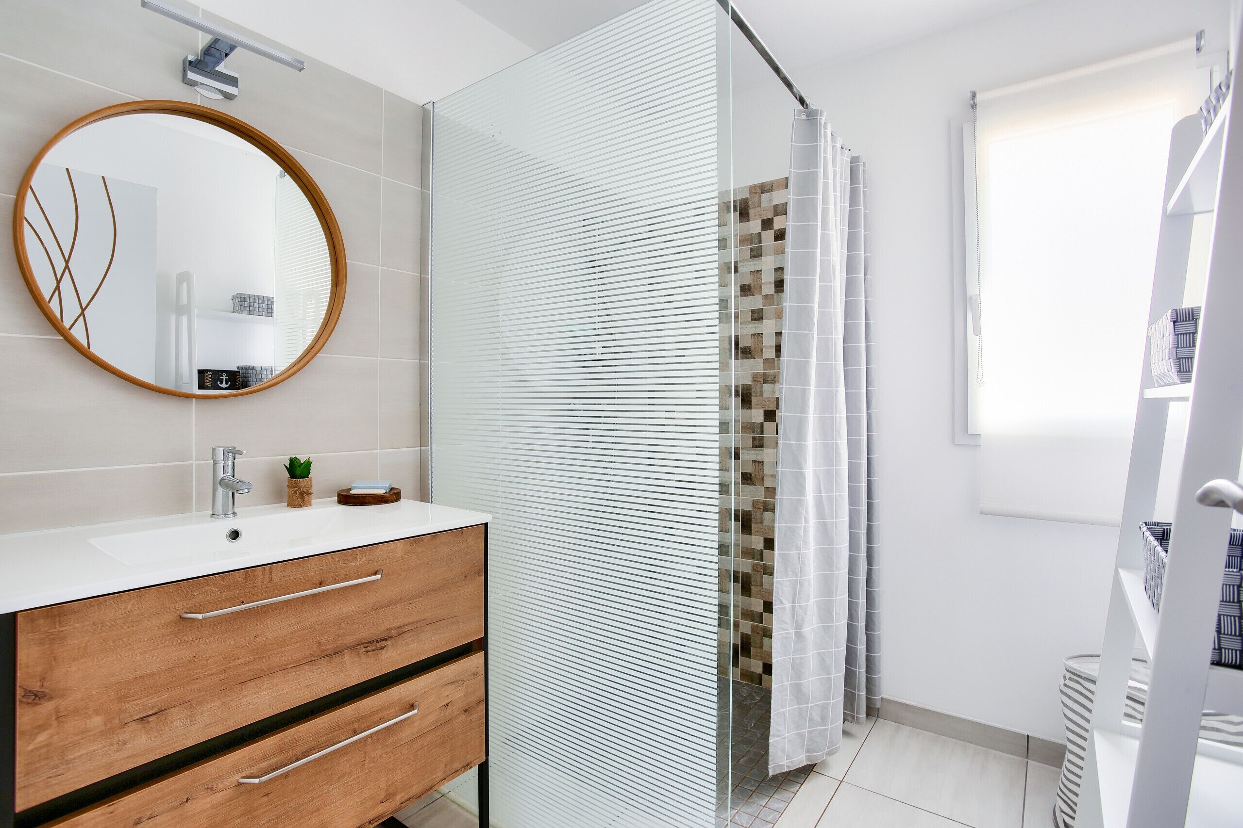 Une salle de bain moderne avec un meuble-lavabo en bois, un miroir rond et une cabine de douche en verre.