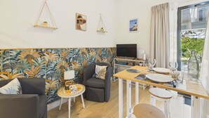En moderne stue med sofa, stole, et lille bord med bakke, et fjernsyn og en balkon med gardiner.