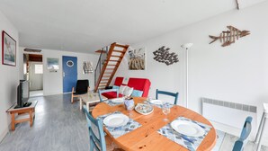 Uma sala de jantar com uma mesa de madeira posta para quatro pessoas, uma escada e um sofá vermelho.