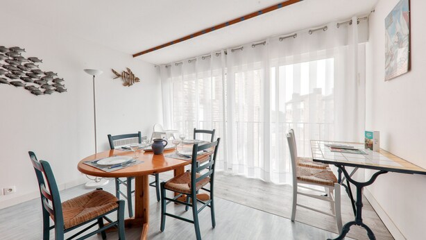Uma área de refeições com uma mesa de madeira redonda, quatro cadeiras e um abajur moderno.