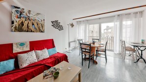 Um quarto com um sofá vermelho, uma mesa de jantar com cadeiras, uma janela grande com cortinas e um quadro na parede.