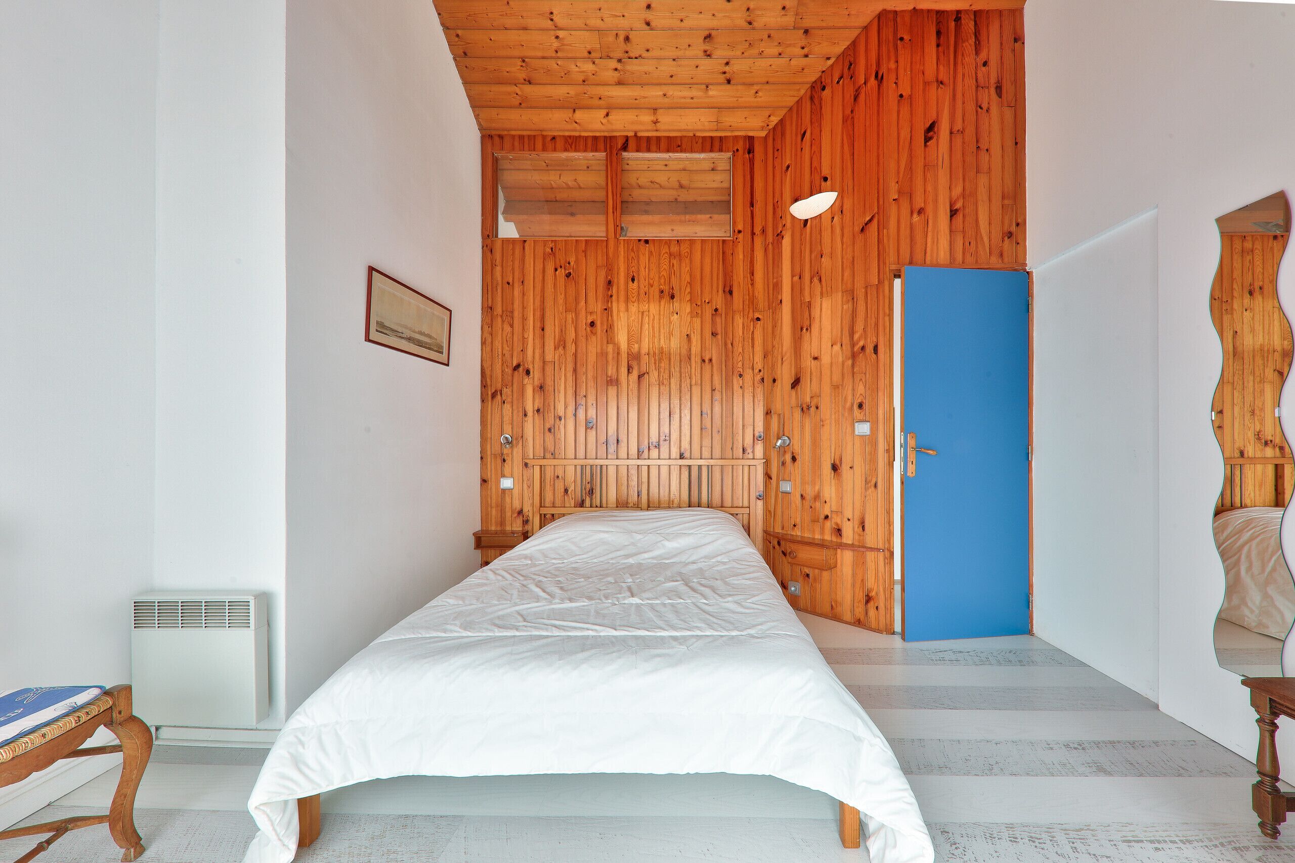 Ein Schlafzimmer mit Holzboden, einer blauen Tür und einem weißen Bett.