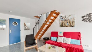 Uma sala de estar moderna com escada de madeira, um sofá vermelho, uma poltrona preta e uma mesa de centro.