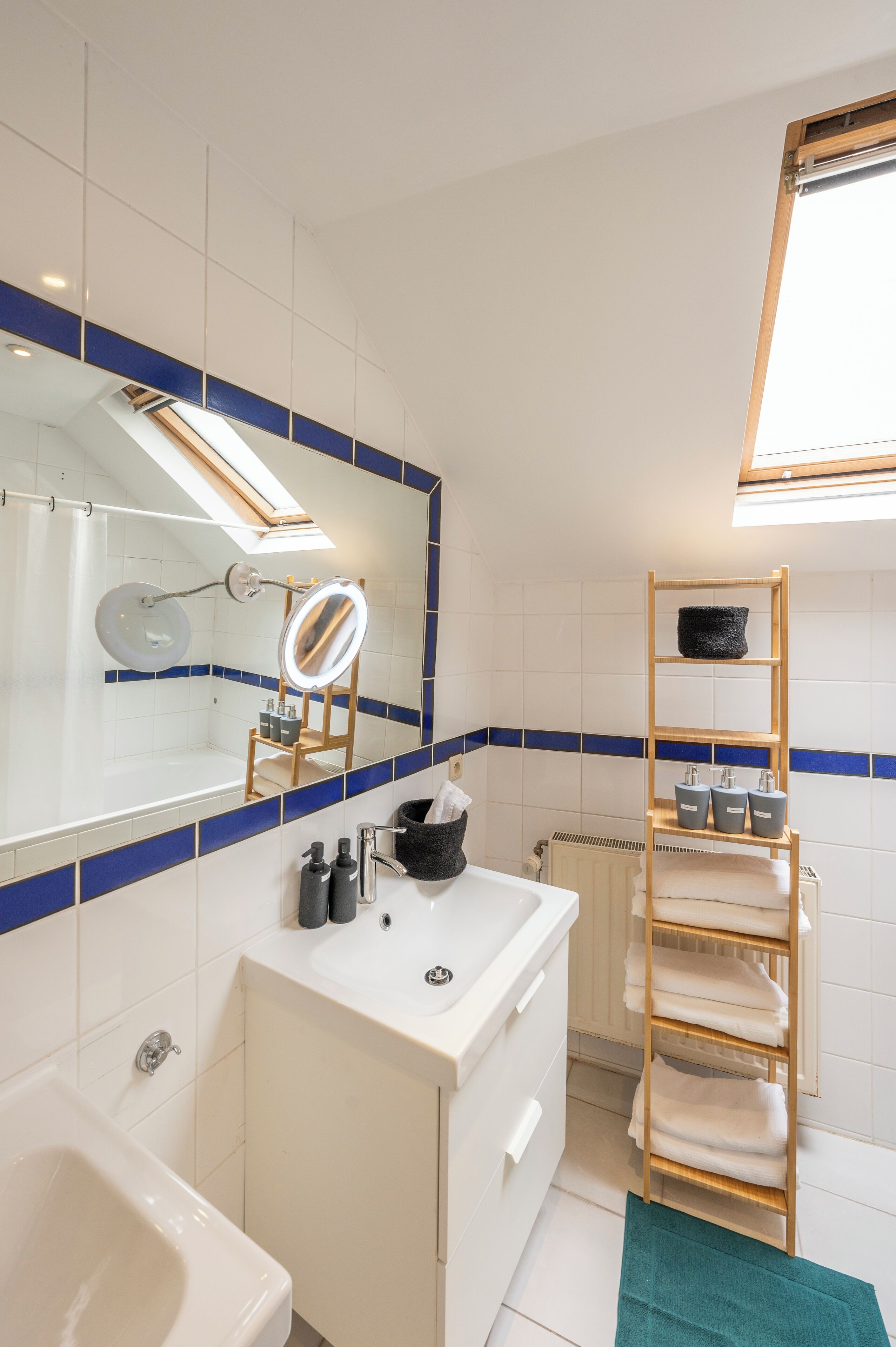 Een moderne badkamer met een grote spiegel, witte tegels, een houten plank en een radiator.