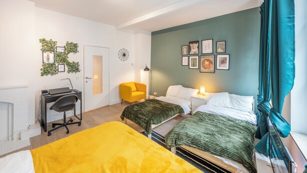 A bedroom with two beds, a desk, a chair, and a wall decorated with framed pictures. - Luminous Suite In Brussels - Elegant Design (Bruxelles)