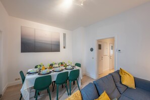 Un comedor con una mesa preparada para cuatro personas, sillas verdes y un sofá gris con cojines amarillos.