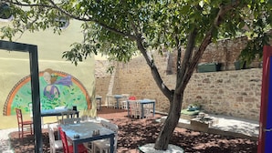 A courtyard with outdoor seating, a mural, and a tree. - Latibule Macaron Guest House (Ayvalik)