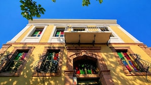 A building with a yellow facade, arched windows, and a balcony with wrought iron railings. - Latibule Macaron Guest House (Ayvalik)